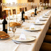 A table setting displaying mini cross rosary favors for guests on a white tablecloth.