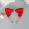 A pair of red plush fox ears headband with black strings displayed on a gray surface.