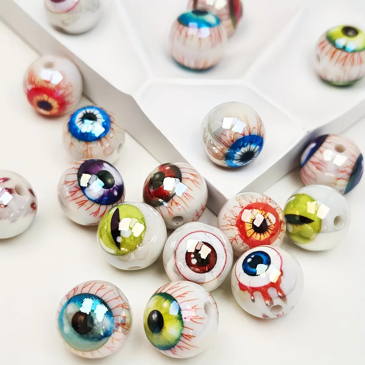 A collection of glossy, double-sided eyeball beads in various colors and designs arranged in a white tray.