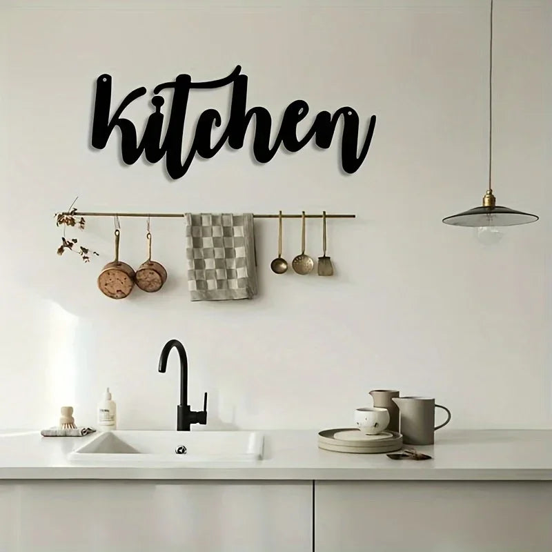 Black script wall art spelling kitchen above a kitchen faucet and hanging utensils on a rack