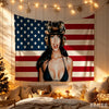 A woman wearing a military helmet poses in front of a large American flag tapestry decorated with stars and stripes.