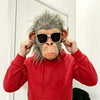 A person wearing a red hoodie holds up a realistic chimpanzee latex mask for cosplay.