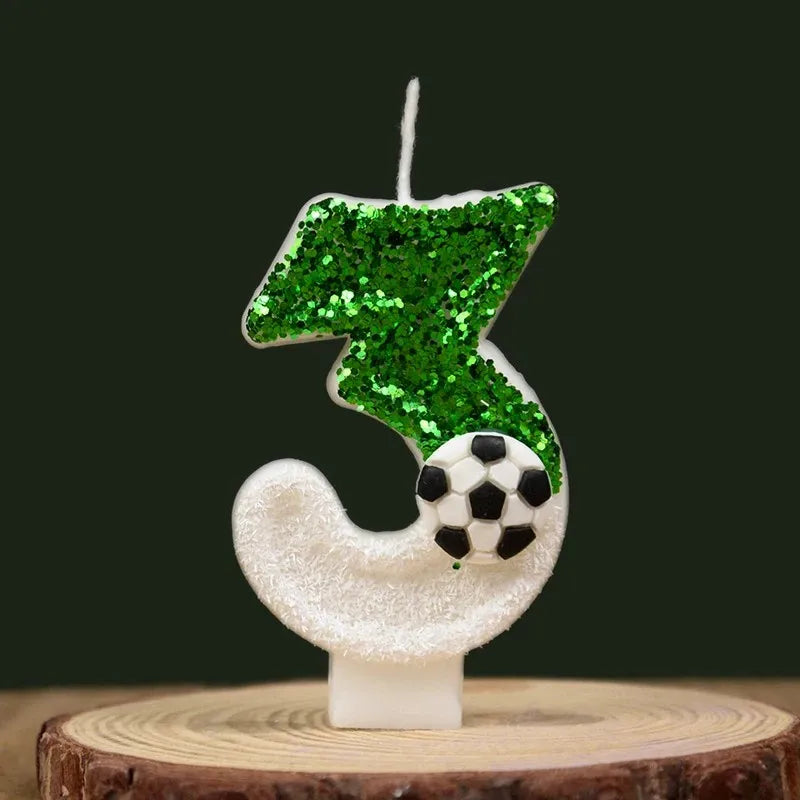 A decorative candle shaped like the number 3, featuring green glitter and a soccer ball design.