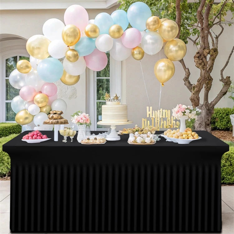 A black stretch rectangle tablecloth is set up outdoors with a balloon arch and various treats.