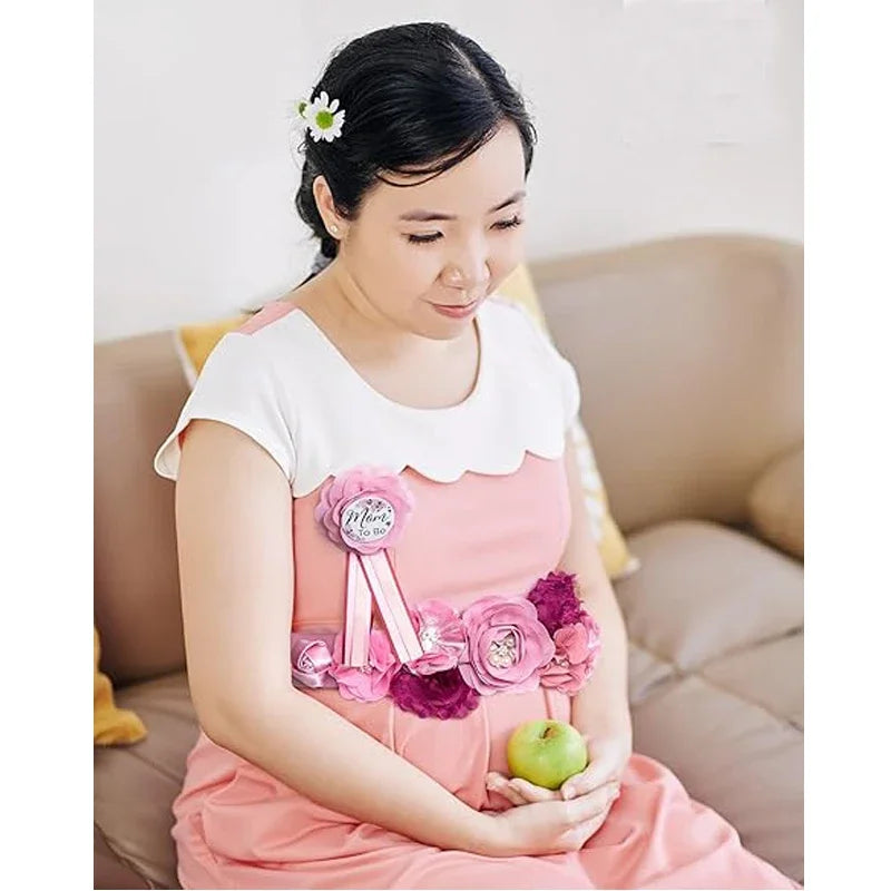 A woman wearing a pink maternity dress is holding a floral sash and corsage pin set.