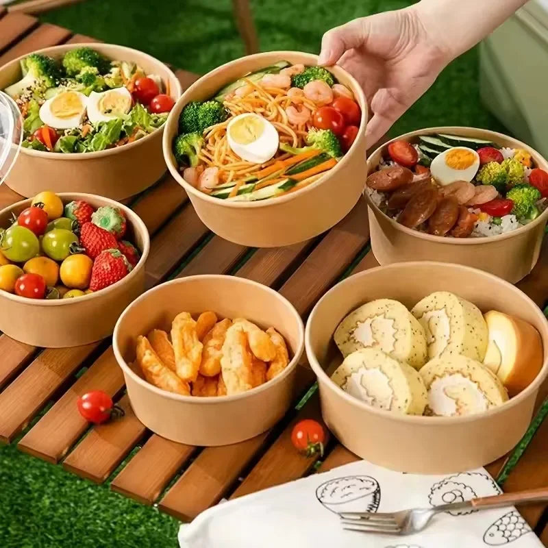 A collection of food items like eggs, vegetables, and fried food served in eco-friendly kraft paper bowls on a wooden surface