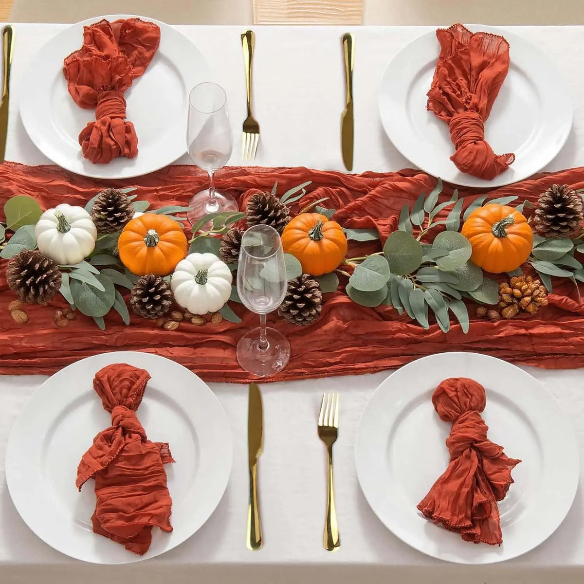 A table setting featuring terracotta semi-sheer cheesecloth napkins and a rust-colored runner with seasonal foliage and pinec
