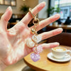 A hand holds a gold-colored crystal heart rhinestone keychain and bag charm.