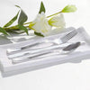 A set of gold disposable cutlery including forks, spoons, and knives placed on a white napkin with a white rose.