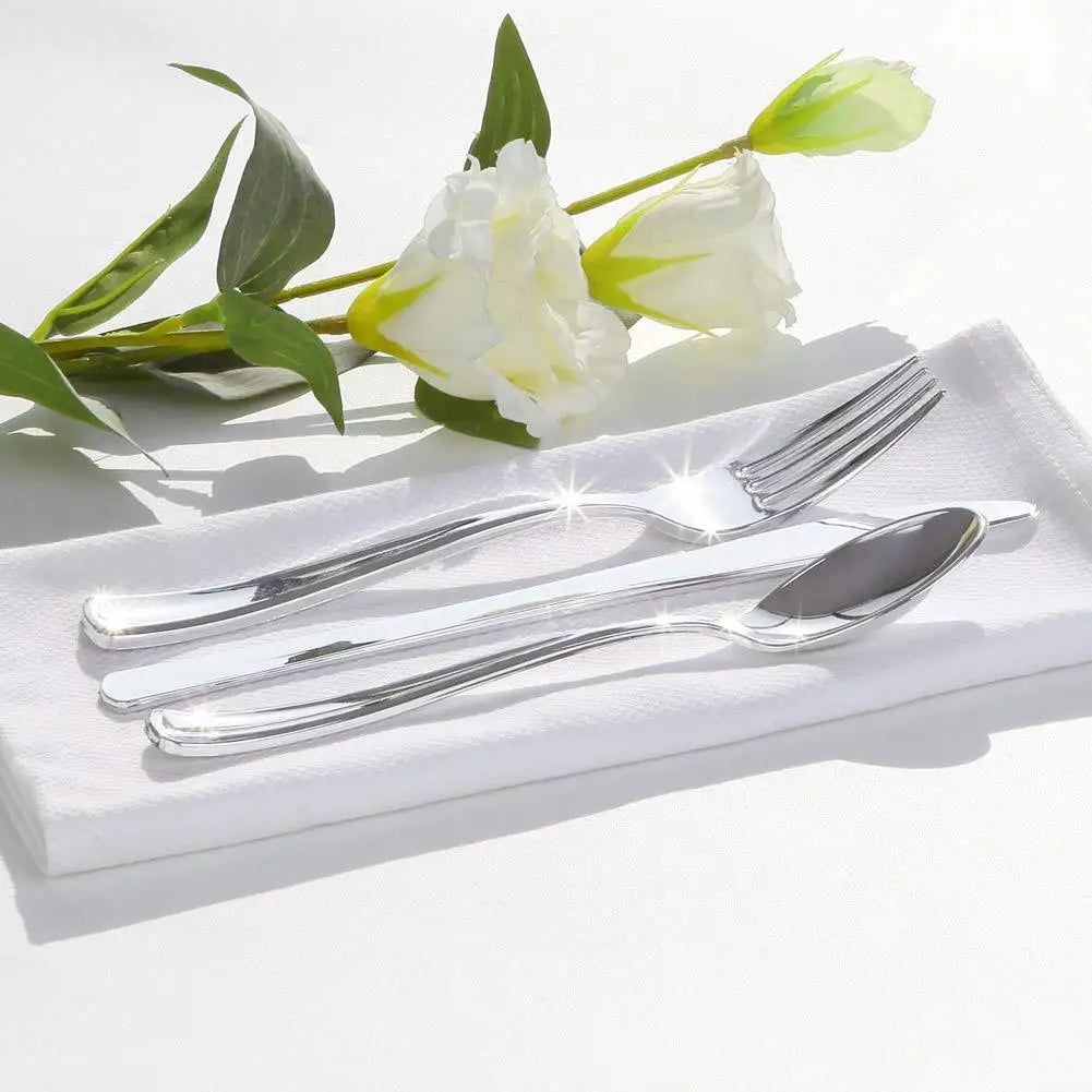 A set of gold disposable cutlery including forks, spoons, and knives placed on a white napkin with a white rose.