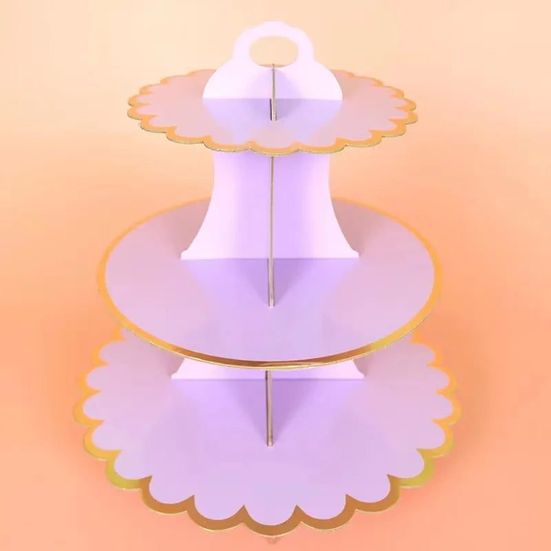 A three-tier rainbow cupcake stand with gold accents displayed on a light orange background.