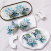 A set of six dusty blue silk rose boutonniere floral accessories displayed on a white marble surface.