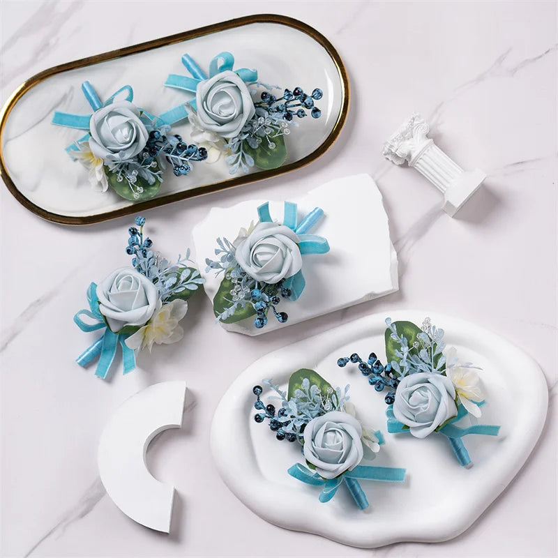 A set of six dusty blue silk rose boutonniere floral accessories displayed on a white marble surface.