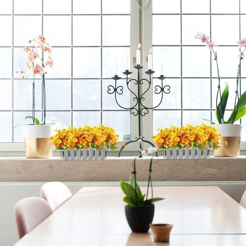 A floral arrangement featuring pink and yellow artificial daisy flowers displayed on a windowsill with candelabras.