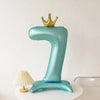 A teal foil balloon shaped like the number one with a gold crown on top.