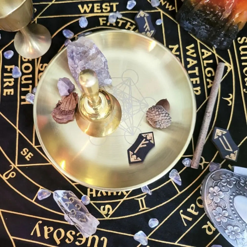 A brass pentagram altar plate with crystals, wood, and dark stones set on a black background.