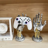 A white and silver 3D gamepad controller is displayed next to a metallic hand puppet, set in a wooden storage box.