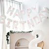 A white balloon banner spelling out Happy Birthday strung across a window with sheer curtains.