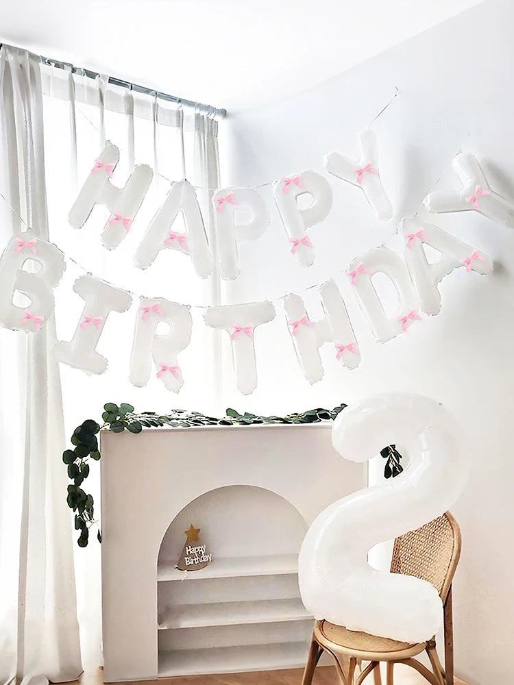 A white balloon banner spelling out Happy Birthday strung across a window with sheer curtains.