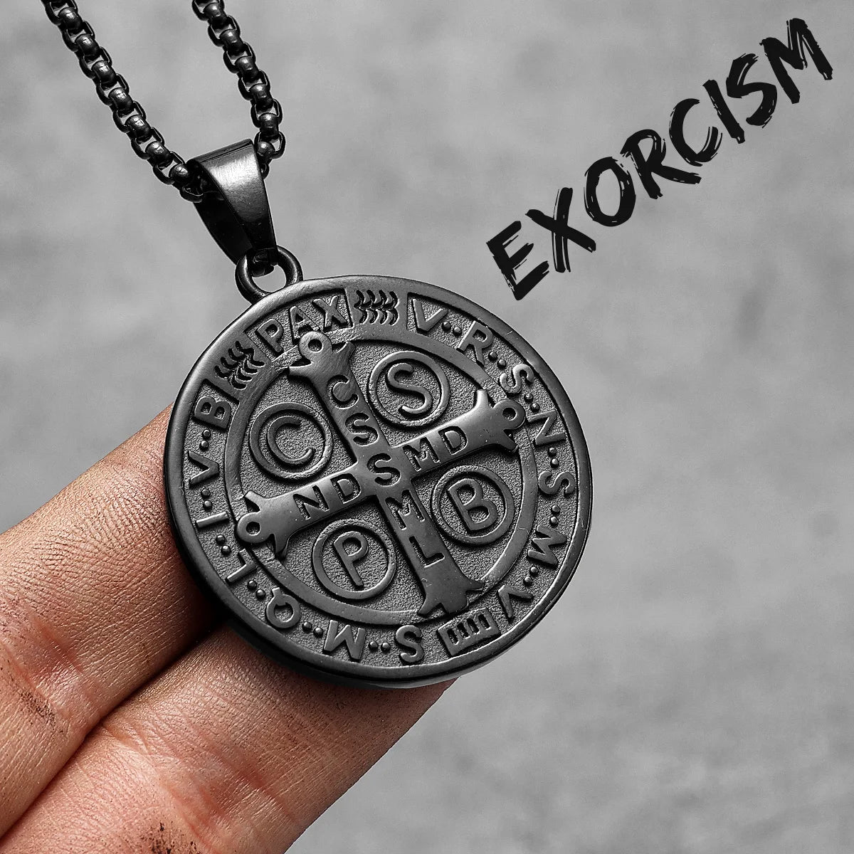 A stainless steel punk cross necklace with an oval pendant featuring Latin text and a chain, held in a hand.