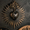 A dark metal wall plaque featuring a sunburst design with rays radiating from a heart shape.