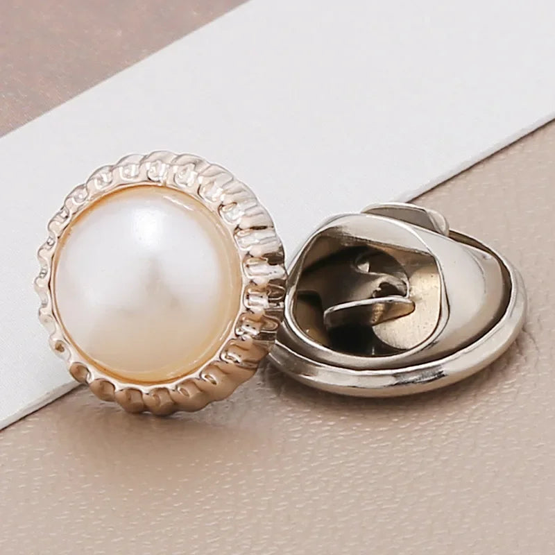 A close-up of a pearl button with a silver setting and rhinestone detail resting on a white card.