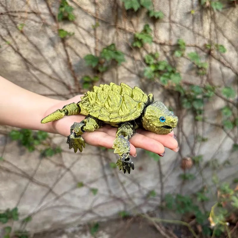A hand is holding a green 3D printed alligator snapping turtle figurine with articulated joints against a blurred natural bac