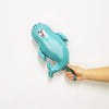 A teal foil balloon shaped like a sea turtle with a face, being held against a white wall.