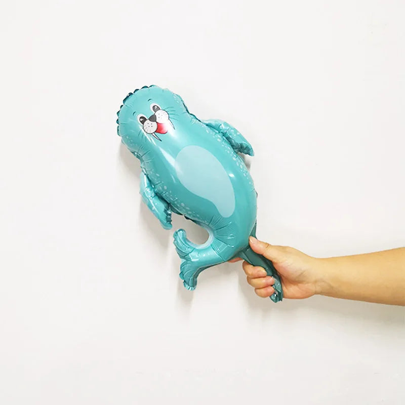 A teal foil balloon shaped like a sea turtle with a face, being held against a white wall.