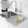 A silicone drain mat is placed on a kitchen sink, showing water flowing through the faucet and citrus fruit.