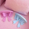 Two pink and blue decorative bow-shaped wooden wall shelves resting on a pink fabric surface.