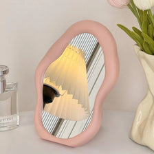A pink cloud-shaped folding mirror with a light-colored, striped shade is displayed on a white surface.