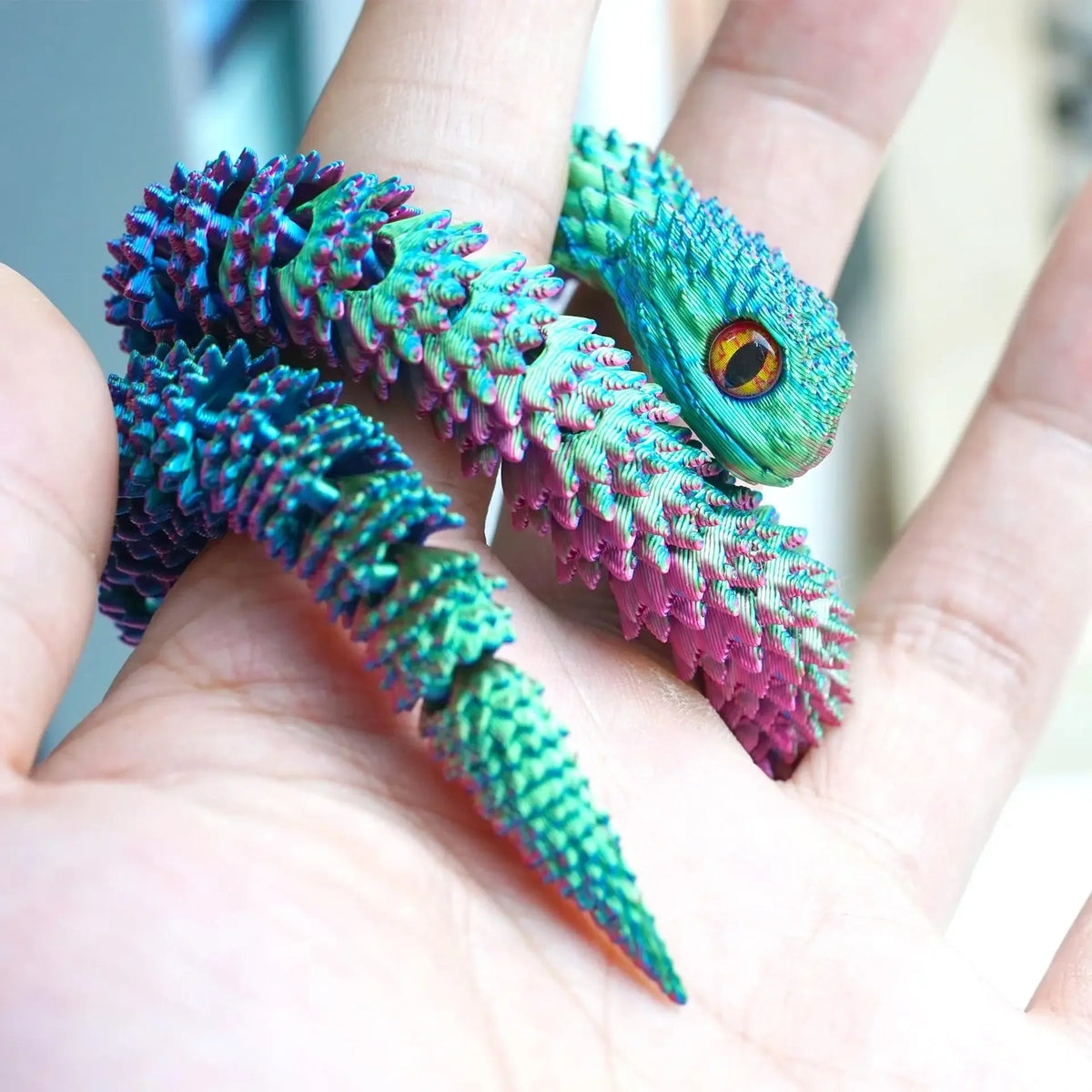 A hand holds a vibrant, textured 3D printed articulated snake fidget toy with iridescent green and purple scales.