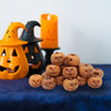 A collection of small, carved resin pumpkins in various shades of orange and brown displayed next to a lit candle.