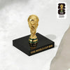 A gold-colored FIFA World Cup 2026 trophy figurine displayed on a black square base.