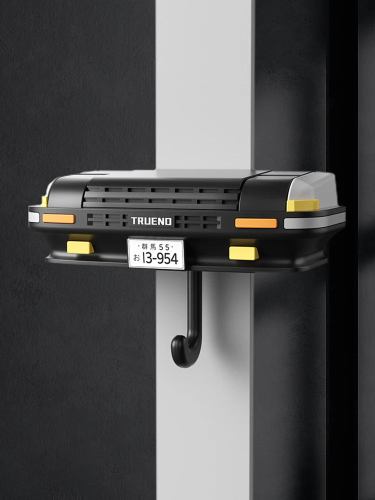 A black classic car headlight key holder with an LED illumination feature mounted on a white wall.