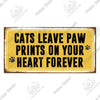 A rustic yellow wooden sign with black text that reads Cats leave paw prints on your heart forever.