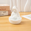 A white resin statue of the Virgin Mary with a veil and halo, placed on a wooden table next to books.