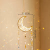 A hanging gold crescent moon dreamcatcher with dangling crystal beads and a rainbow prism.