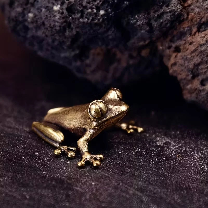 A vintage brass frog statue desktop ornament resting on a dark, textured surface.