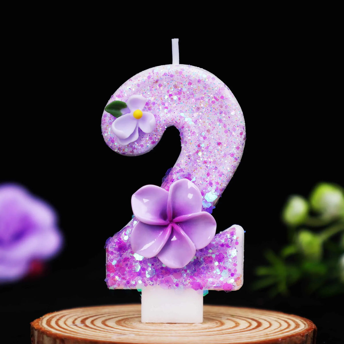 A purple glitter number candle shaped like the number 2, decorated with a purple flower.