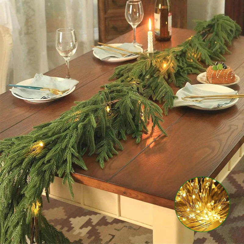 Green Norfolk pine Christmas garland with warm lights draped across a wooden table.