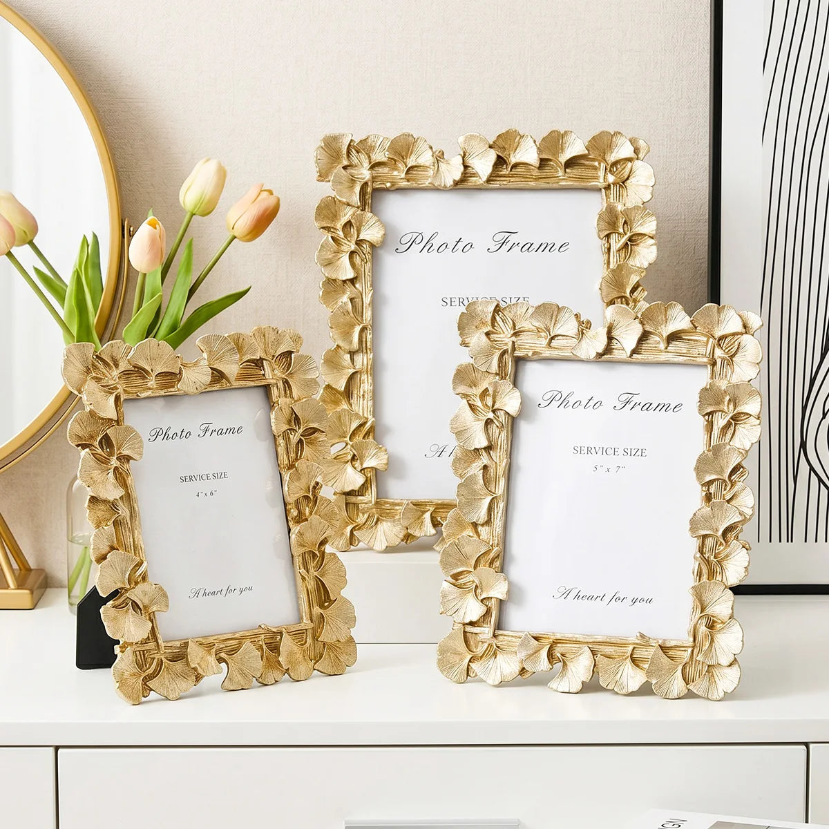 A set of three gold leaf picture frames with white mats and floral borders displayed on a white surface.