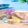 A set of luminous resin mini crab decor in purple, pink, and yellow resting on light sand.
