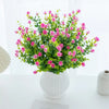 A bouquet of artificial eucalyptus branches with pink flowers and green leaves in a white vase.
