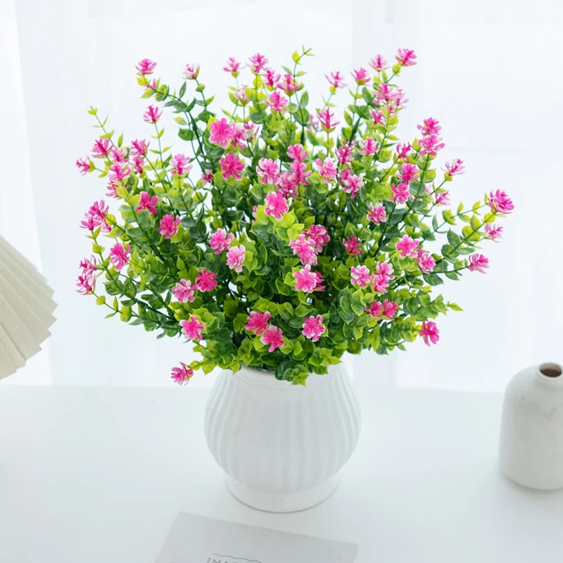 A bouquet of artificial eucalyptus branches with pink flowers and green leaves in a white vase.