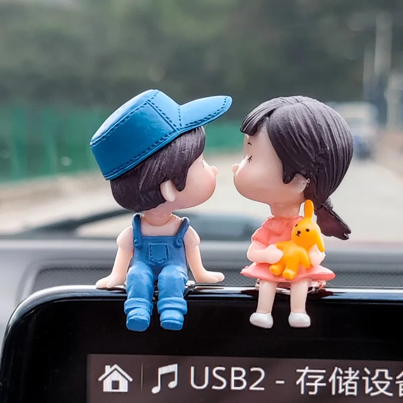 A figurine of a girl and a boy with an orange balloon, displayed on a car dashboard.