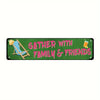 A green metal sign with pink text that reads Gather with Family & Friends and features a depiction of a striped beach chair.