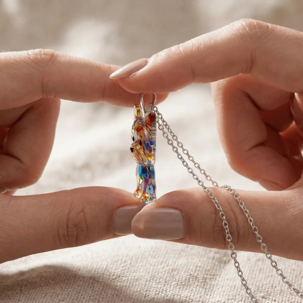A close-up of a hand holding a Yorkshire Terrier acrylic pendant necklace against a neutral background.