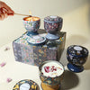 A set of soy wax aromatherapy candles in decorative tins and a lit candle being held by a hand.